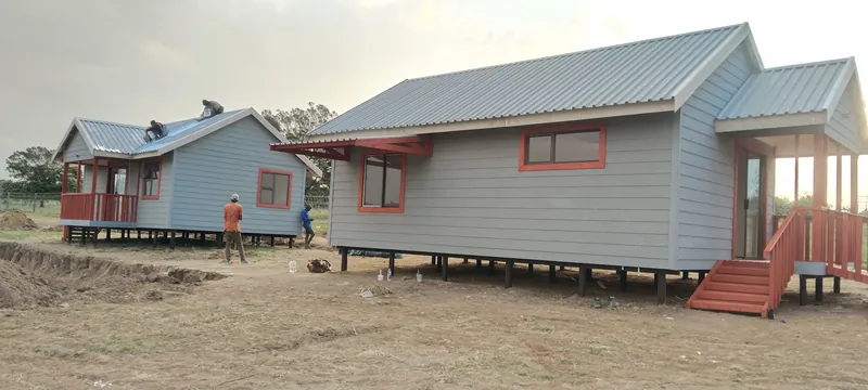 Two grey Nutec homes with red trim raised on timber poles on a building site