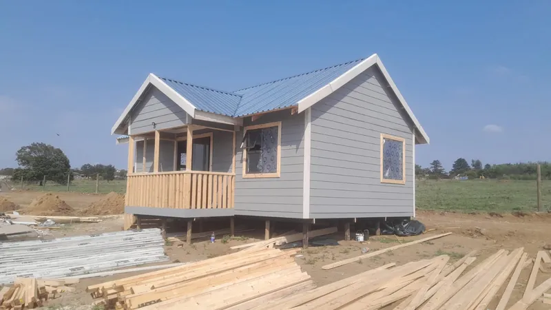 Grey Nutec cottage with a timber veranda and a pitched metal roof, raised on timber poles